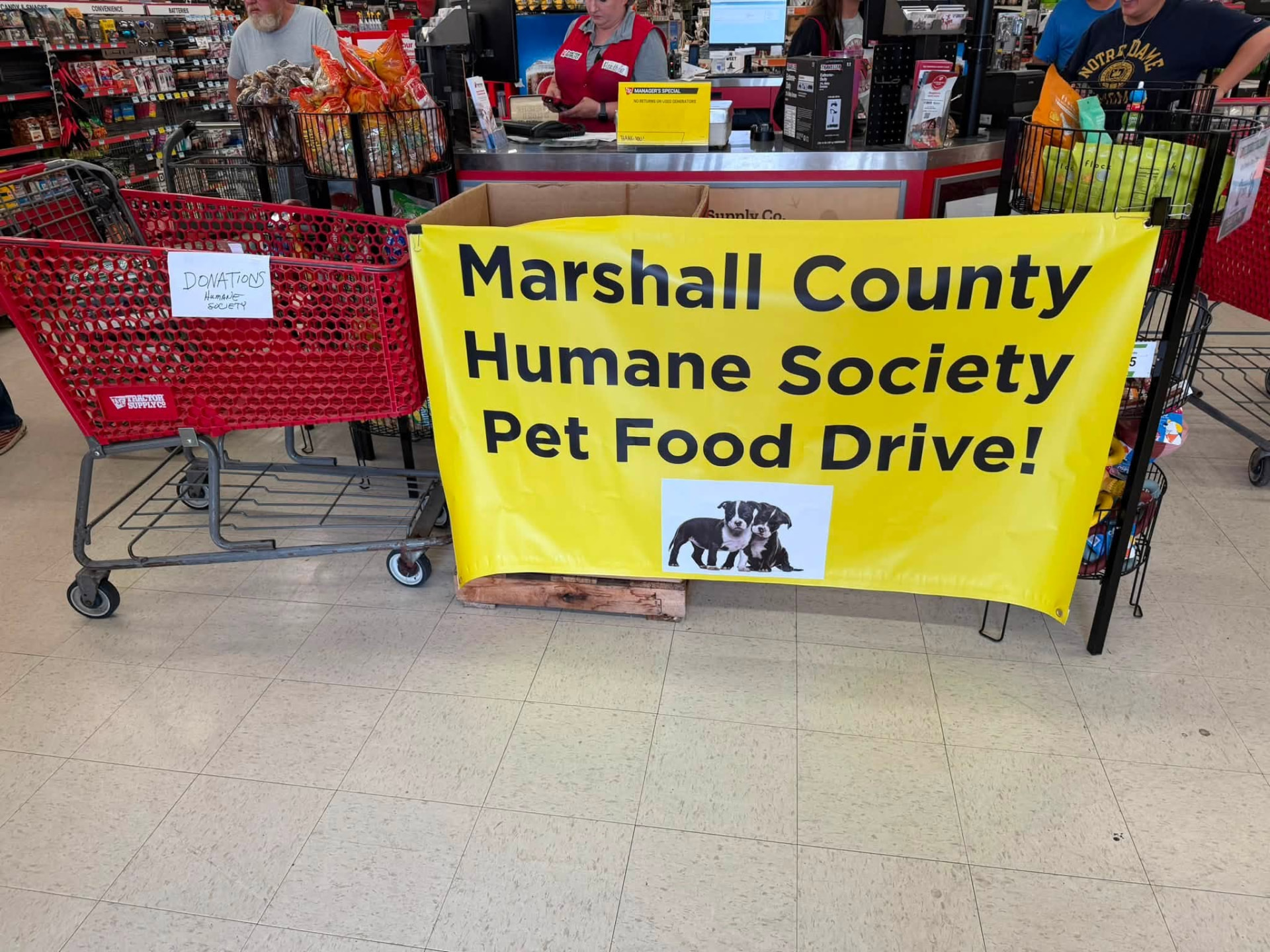 A yellow Marshall County Humane Society Pet Food Drive banner inside Tractor Supply next to a donations cart